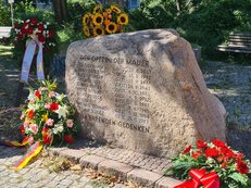 Foto des Gedenksteins für die Maueropfer in der Bernauer Straße umgeben von mehreren Gedenkkränzen.