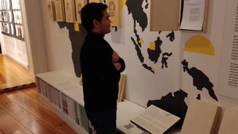 Foto des Bezirksverordneten Samiullah Haidary beim Besuch des Museums der Trostfrauen. Er liest einen Ausstellungstext. Im Hintergrund ist ein Teil der Ausstellung sichtbar – Bleistiftportraits auf Holz die an einer Wand mit einer Weltkarte angebracht sind. 