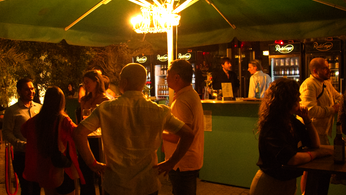 Foto von der Bar des Sommerempfang. In schwummrigen Licht zu sehen sind mehrere kleine Grüppchen und zwei Barkeeper. 