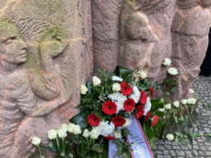 Foto vom Block der Frauen in der Rosenstraße. Angelehnt an die Statuen sind ein Gedenkkranz und weiße Rosen.