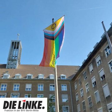 Foto der Progress-Pride Fahne während sie vor dem Rathaus Tiergarten gehisst wird vor einem blauem Himmel.