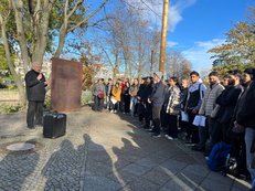 Foto der Gedenkenveransttaltung beim am Sigmundshof in Moabit. Es ist eine große Menschenansammlung zwischen bei der metallenen Gedenktafel abgebildet. Hören einem älteren Mann bei einer Rede zu. 