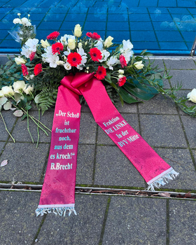 Foto des Gedenkkranzes der Fraktion DIE LINKE. in der BVV Mitte vor dem Mahnmal für die Euthanasieopfer der „T4-Aktion“. Rote und Weiße Blumen, auf einer Schärpe am Kranz steht „Der Schoß ist fruchtbar noch, aus dem es kroch!“ - B. Brecht