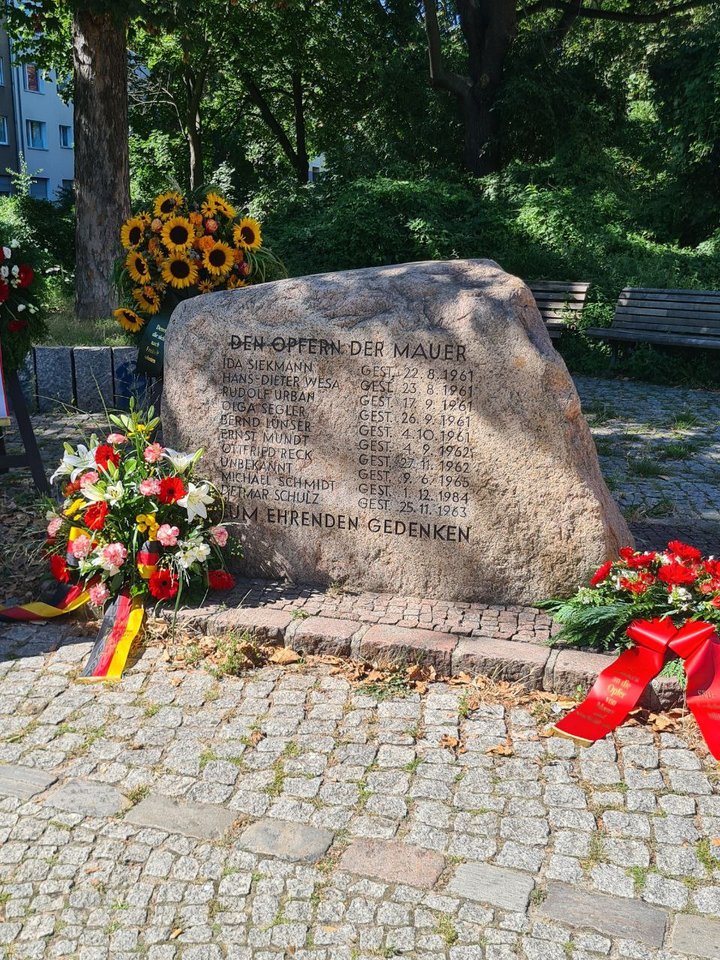 Foto des Gedenksteins für die Maueropfer in der Bernauer Straße umgeben von mehreren Gedenkkränzen.