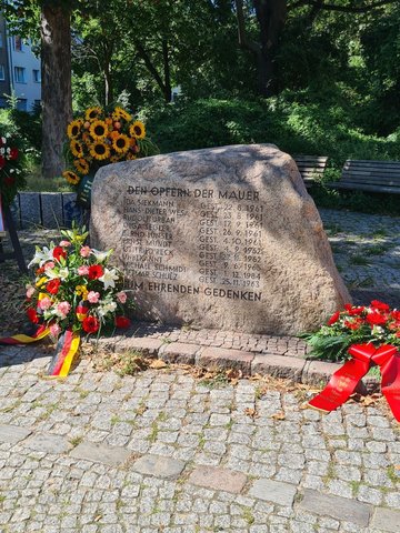 Foto des Gedenksteins für die Maueropfer in der Bernauer Straße umgeben von mehreren Gedenkkränzen.